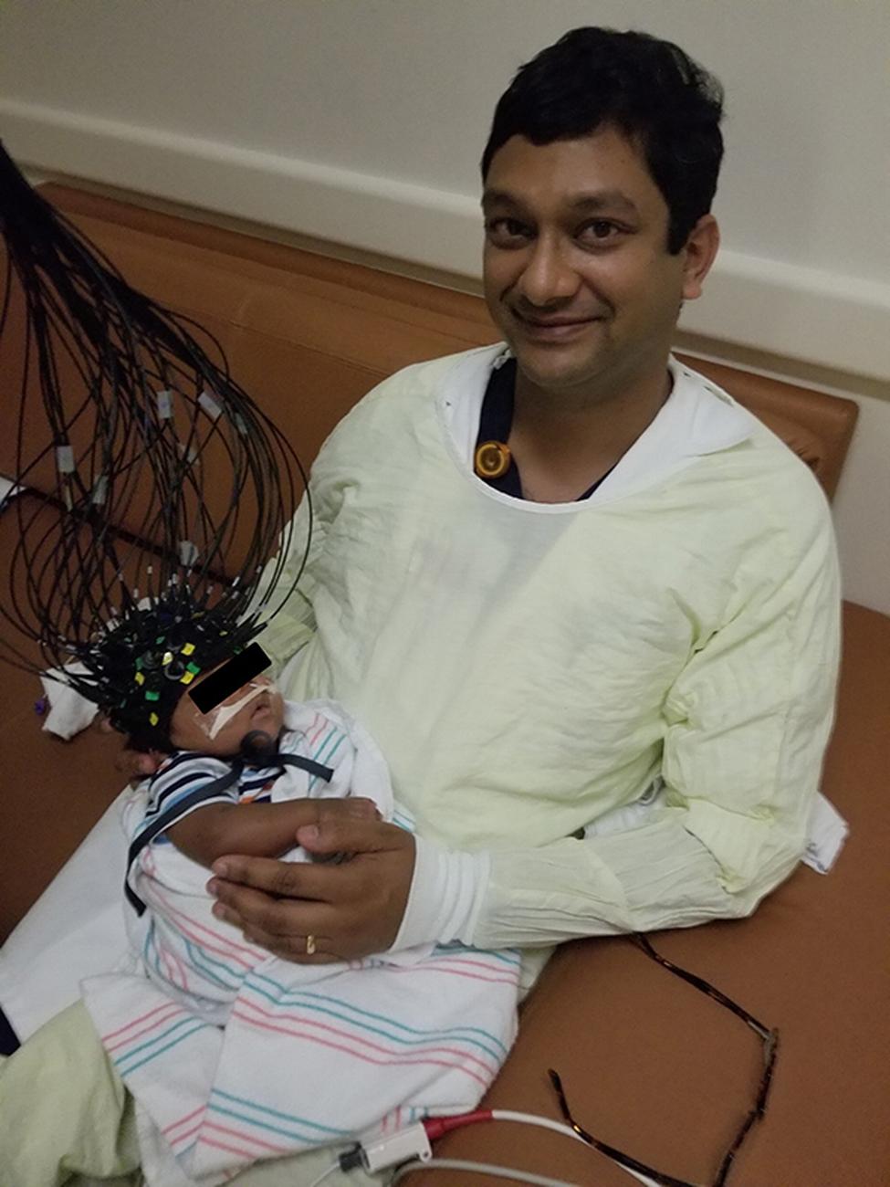 共同领导的研究员Manish N. Shah，医学博士持有患者，而基于CAP的经颅光学层析成像（CTOT）设备的早期版本可在几分钟内捕获全脑成像。（照片由马里兰州的Manish N. Shah提供）